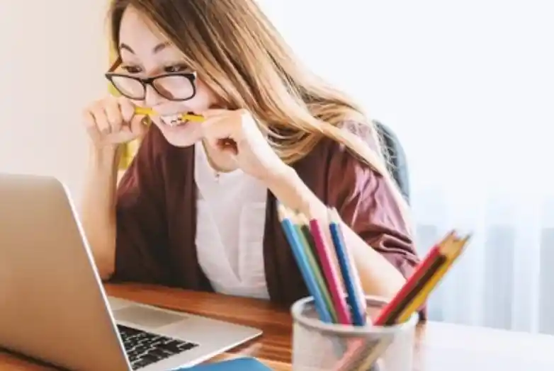 woman sitting behind laptop biting pencil anxiously